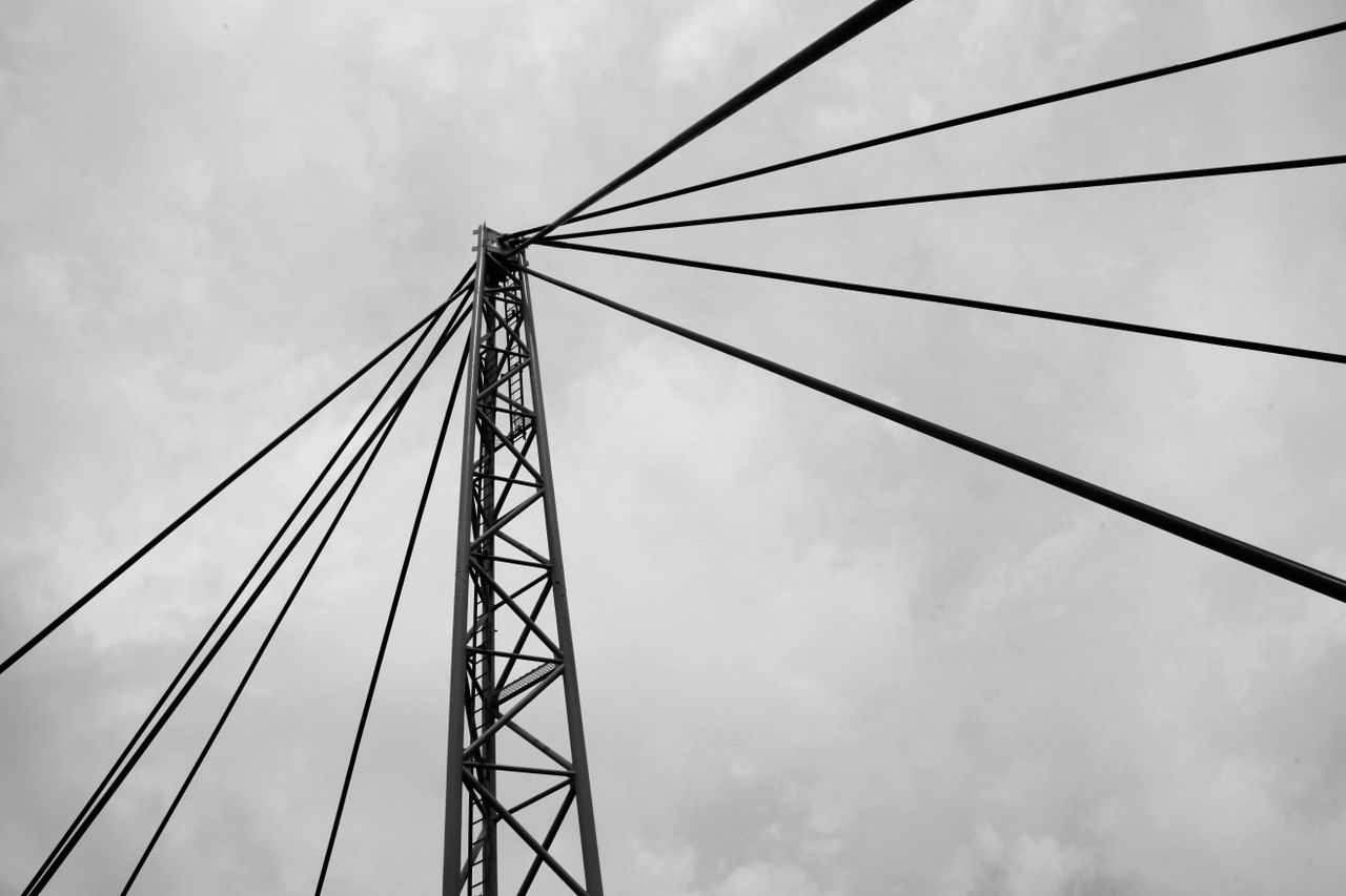 From below black and white modern suspension bridge with main metal cables against gloomy cloudy sky